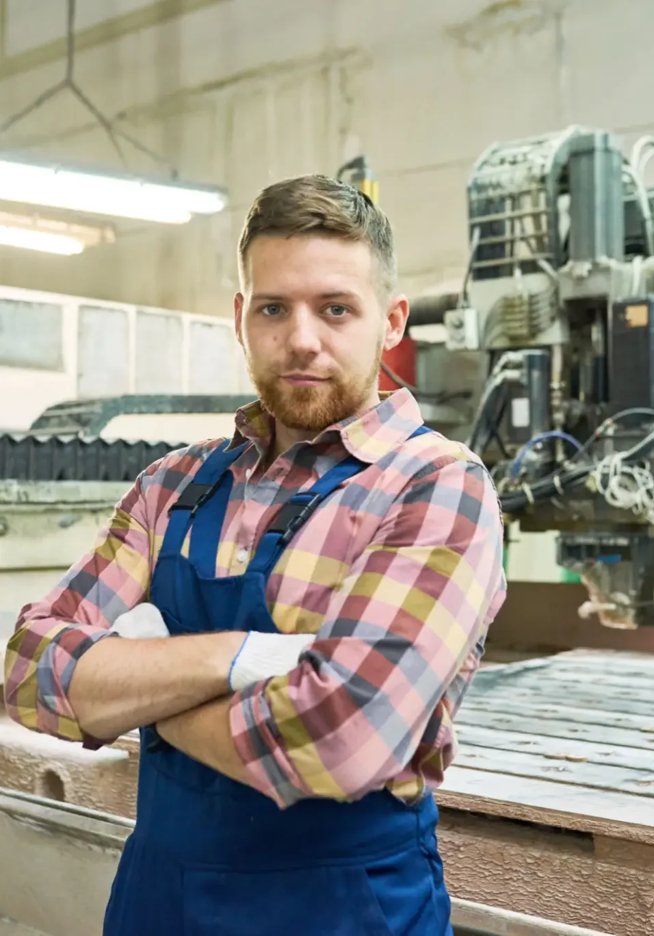Man in a plaid shirt and apron standing confidently in a workshop.
